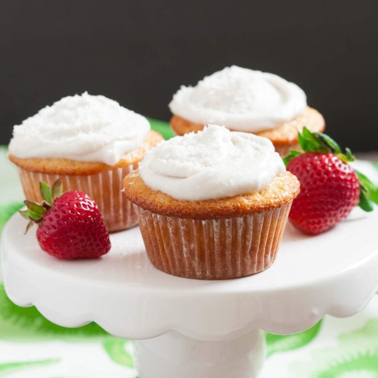 Three dairy free cupcakes with coconut whipped cream on top.