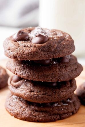 A stack of four double chocolate chip cookies on a wooden surface.