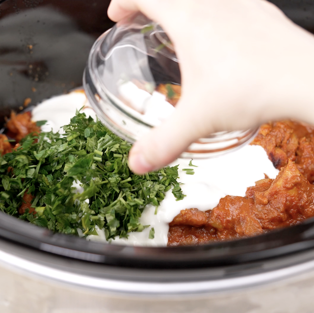 Reserved yogurt and cilantro being added to a slow cooker to make chicken tikka masala.