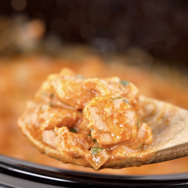 Closeup shot of a wooden spoon with chicken tikka masala on top.