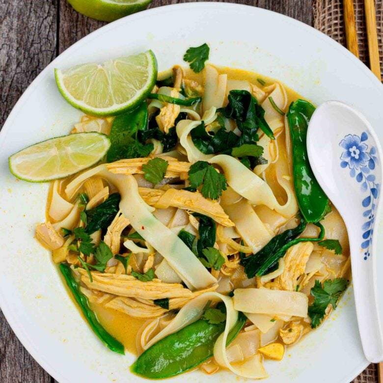 Overhead shot of a plate with coconut chicken curry soup with lime wedges on the side.