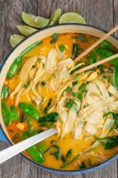 Overhead shot of coconut chicken curry soup in a bowl with lime wedges on the side.