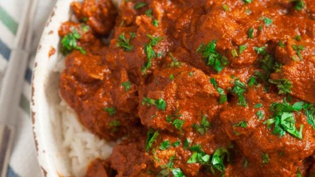 Overhead shot of slow cooker chicken tikka masala with a spoon and fork on the side.