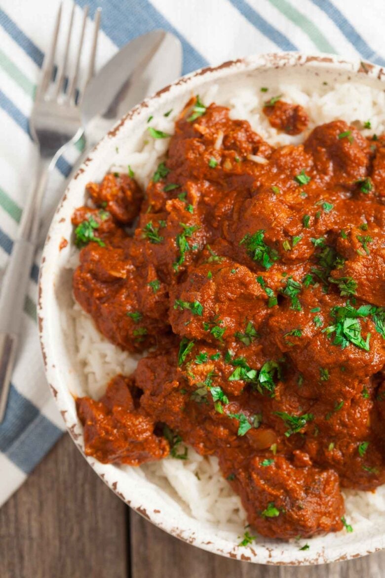 Overhead shot of slow cooker chicken tikka masala with a spoon and fork on the side.