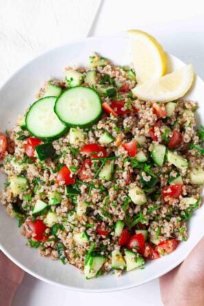 Overhead shot of a hand holding tabbouleh in a white bowl.