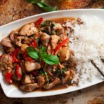Overhead shot of a large plate with thai basil chicken, white rice, and chopsticks on the side.