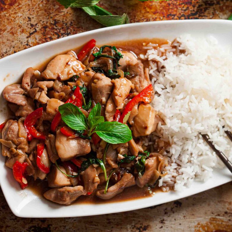 Overhead shot of a large plate with thai basil chicken, white rice, and chopsticks on the side.