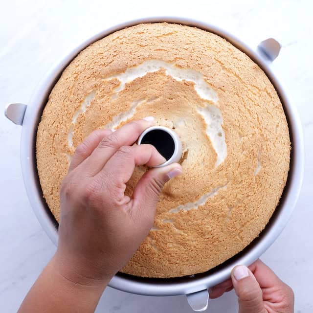 A hand pulling out angel food cake from angel food cake pan.
