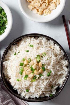 coconut rice topped with macadamia nuts and cilantro in a bowl with chopsticks.