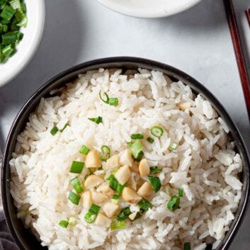 coconut rice topped with macadamia nuts and cilantro in a bowl with chopsticks.