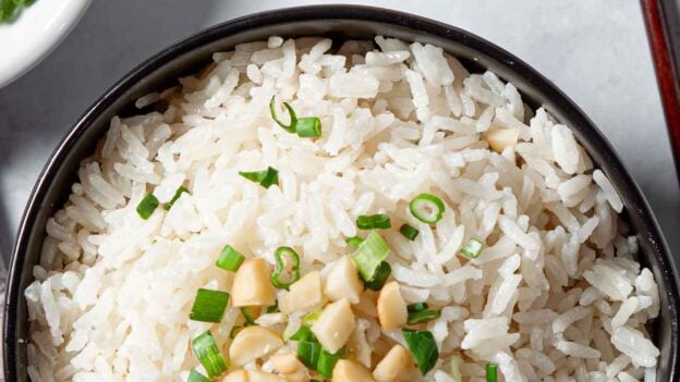 coconut rice topped with macadamia nuts and cilantro in a bowl with chopsticks.