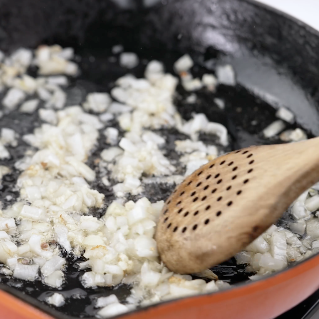 Onion and garlic being sauteed in a pan.