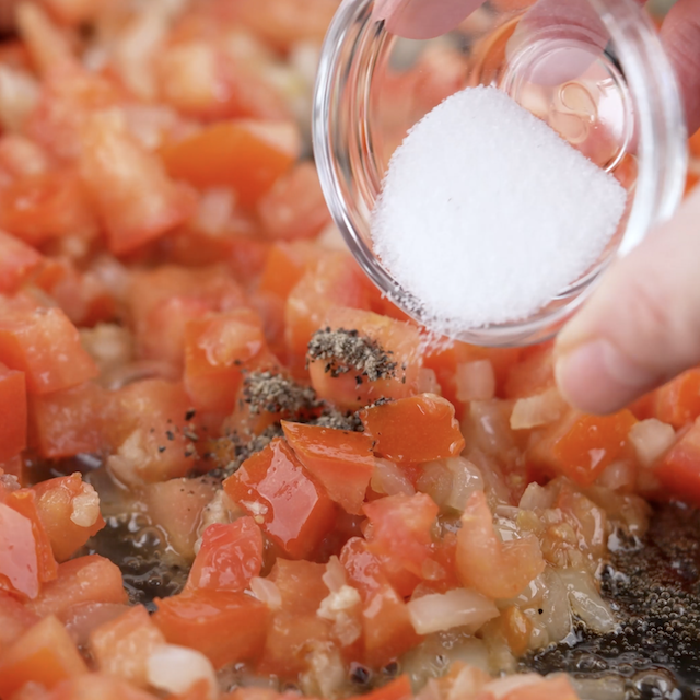 Salt being added to a pan with tomatoes.