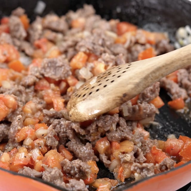Ground cooked sausage being added to a pan.