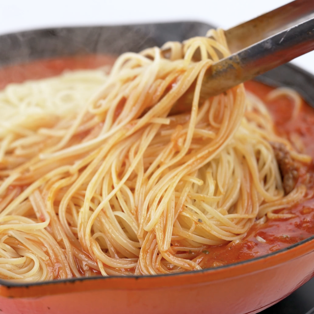 Pasta being tossed with sauce.
