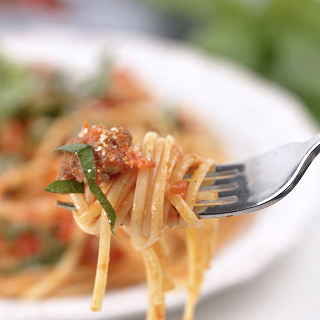 Italian sausage pasta on a fork with fresh herbs on top.