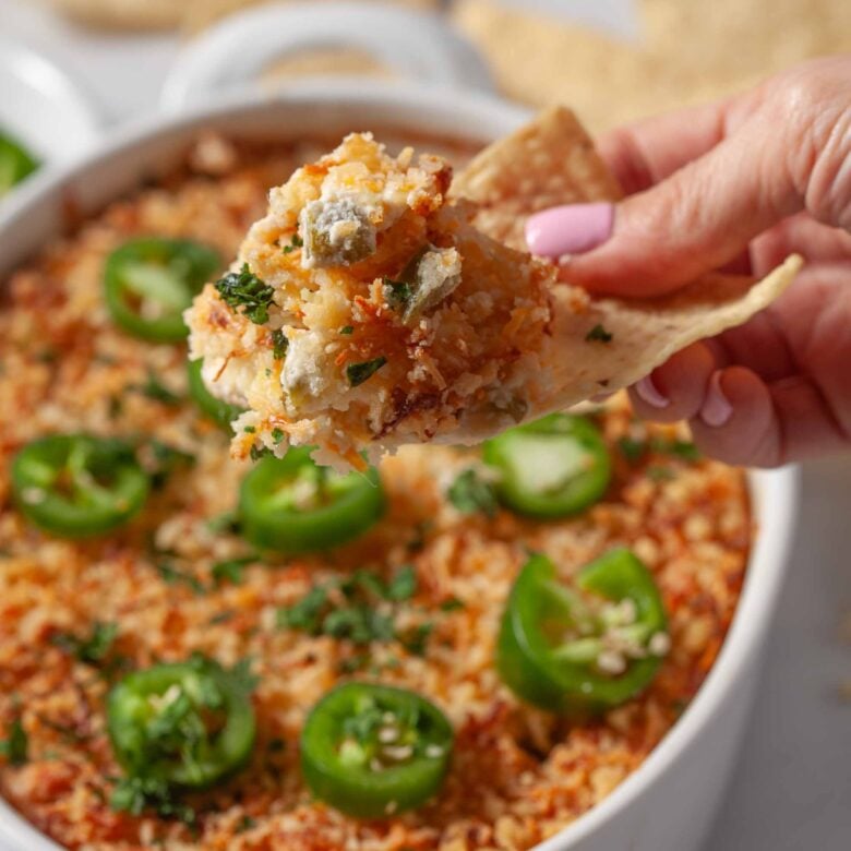 Jalapeño popper dip being scooped with a tortilla chip.