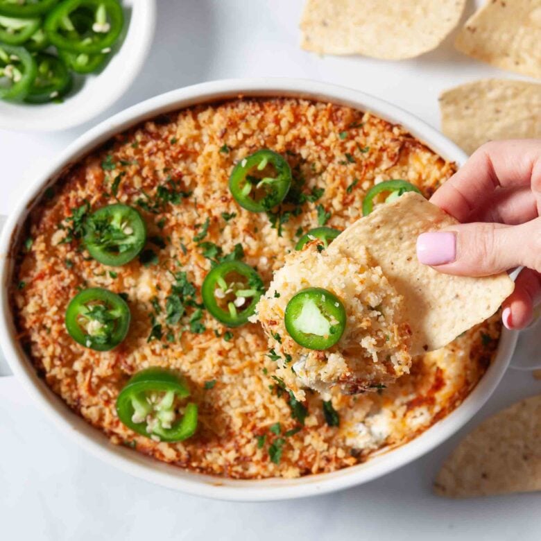 Jalapeño popper party dip being scooped up with a tortilla chip.