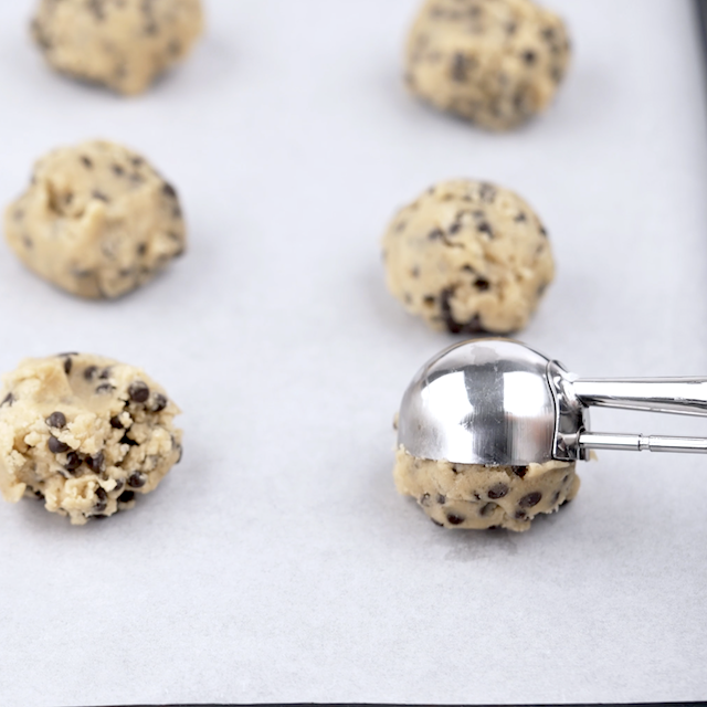 Cookie dough being scooped onto a lined baking sheet.