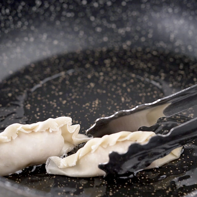 Potstickers being added to a pan with oil.