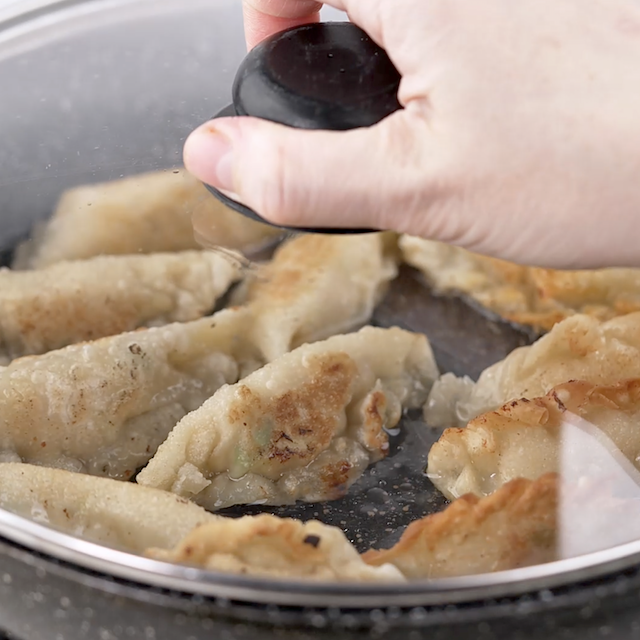 Potstickers in a pan with a lid on the top.