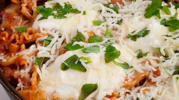 Closeup shot of skillet lasagna in a pan with cheese on top and garnished with fresh herbs.