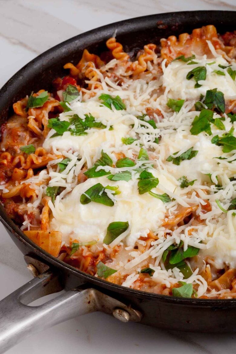 Closeup shot of skillet lasagna in a pan with cheese on top and garnished with fresh herbs.