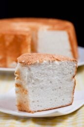 Closeup shot of a slice of angel food cake on a plate with the rest of the cake at the back.
