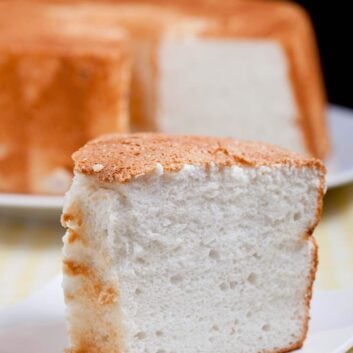Closeup shot of a slice of angel food cake on a plate with the rest of the cake at the back.