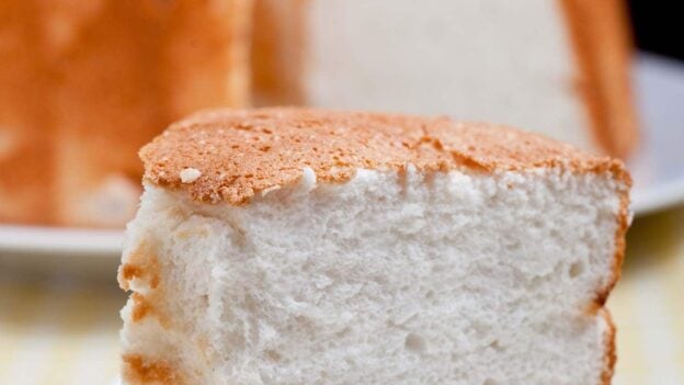 Closeup shot of a slice of angel food cake on a plate with the rest of the cake at the back.