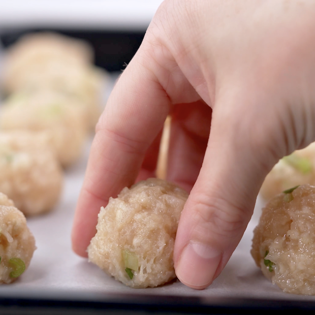 Buffalo chicken meatballs being placed on a lined sheet, ready to bake.