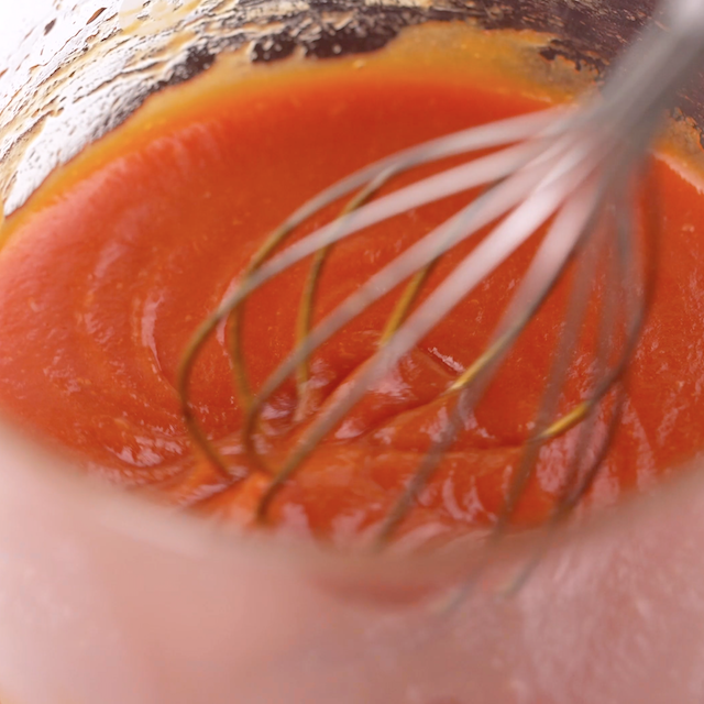 Homemade buffalo sauce being whisked to make buffalo chicken meatballs.
