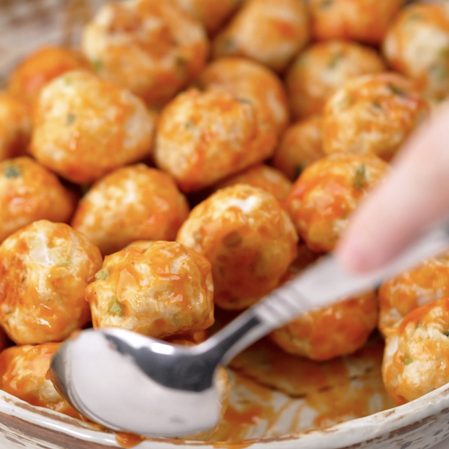 Buffalo chicken meatballs being tossed with homemade buffalo sauce.