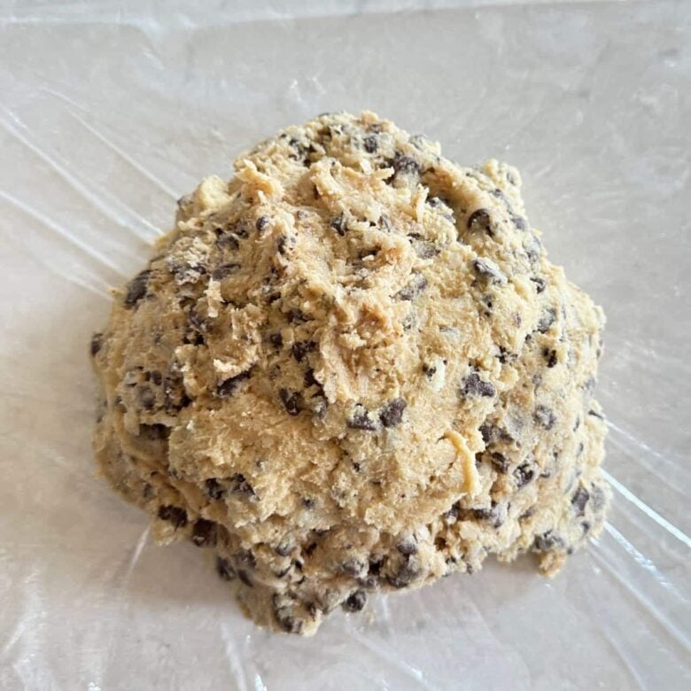 Coconut chocolate chip cookie batter on sheet of cling wrap.