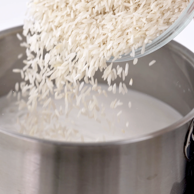 A wooden spoon stirring a white liquid in a stainless steel pot, preparing creamy Coconut Rice.