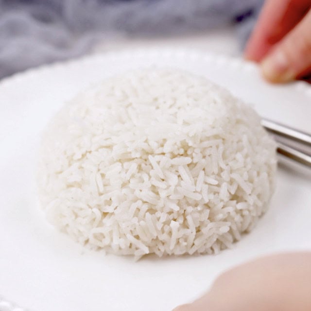 A mound of Coconut Rice, an Asian style dish, is served on a white plate with a fork and spoon beside it.