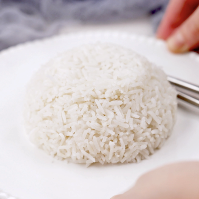 A mound of Coconut Rice, an Asian style dish, is served on a white plate with a fork and spoon beside it.