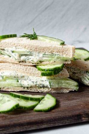 Cucumber Sandwiches cut into triangles shown on a platter, garnished with cucumber slices and lemon slices.
