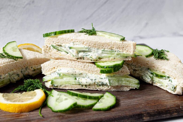 Cucumber Sandwiches cut into triangles shown on a platter, garnished with cucumber slices and lemon slices.