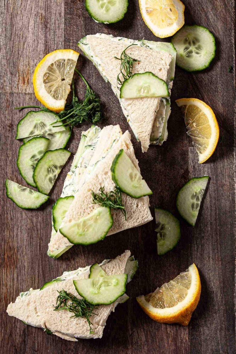 Cucumber Sandwiches cut into triangles shown on a platter, garnished with cucumber slices and lemon slices. 