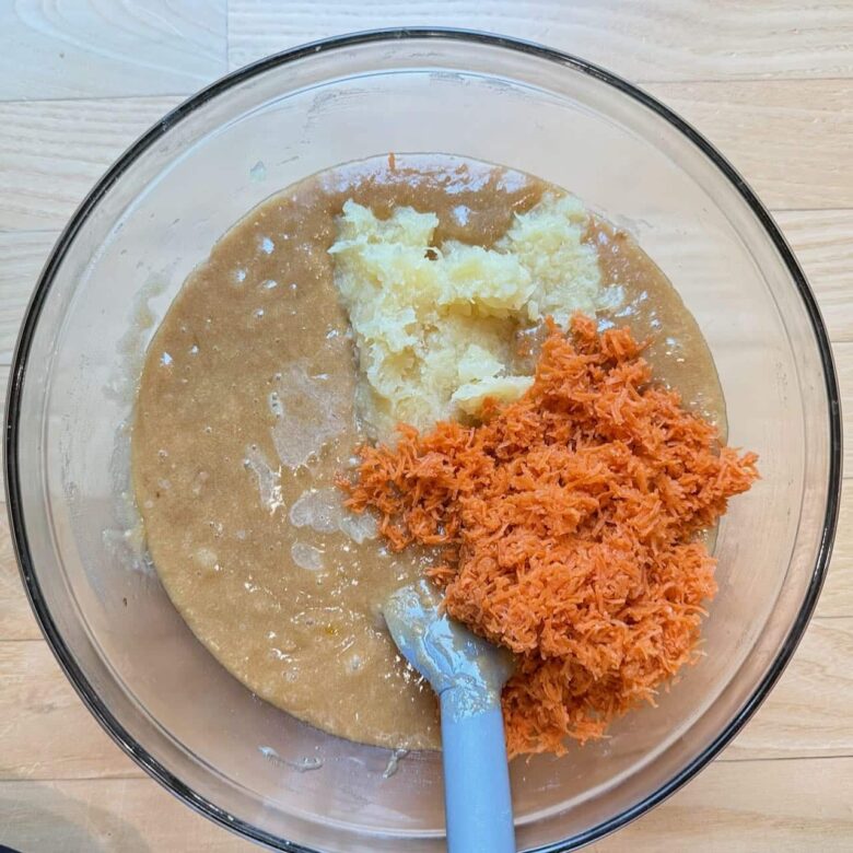 carrot cake batter with carrots and pineapple being added into bowl.