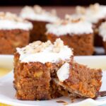 Carrot cake with cream cheese frosting sliced into a square piece and a fork digging into it.