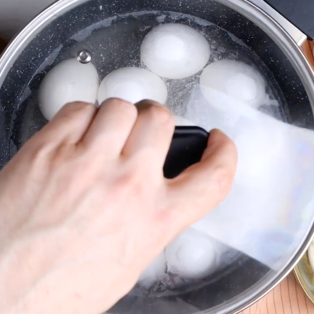 A hand putting a lid on a pot with eggs.