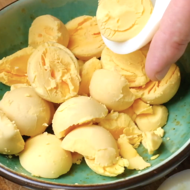 Egg yolks being scooped out into a bowl to make deviled eggs.