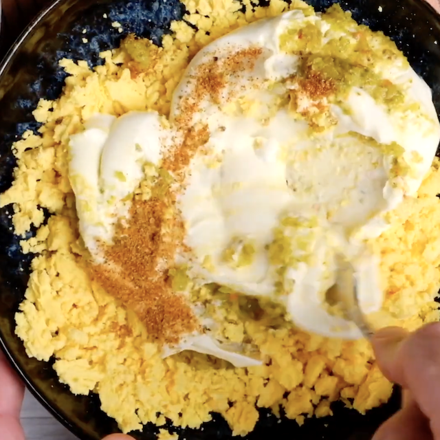 Mayo, seasoning, and mustard being mixed into mashed yolks to make deviled eggs.