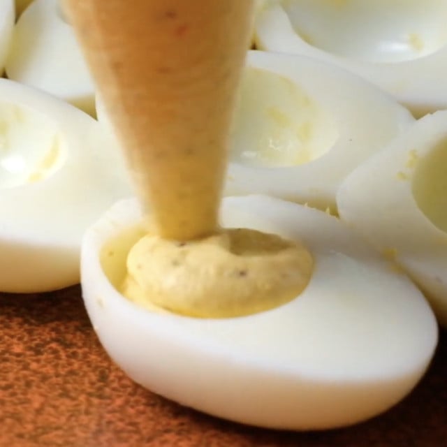 Deviled eggs mixture being piped into cooked, egg whites.