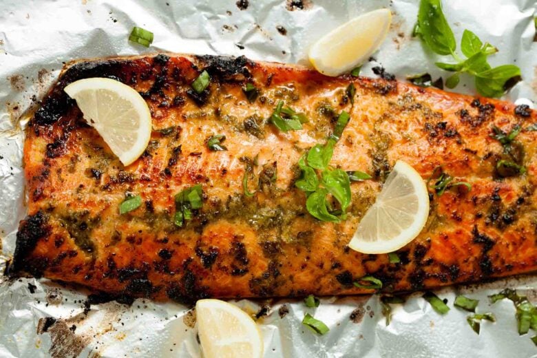 A wooden spoon spreads a herb and oil marinade over a raw salmon fillet on a sheet of aluminum foil, perfect for an easy 30 minute dinner or as part of your go-to salmon recipe collection.