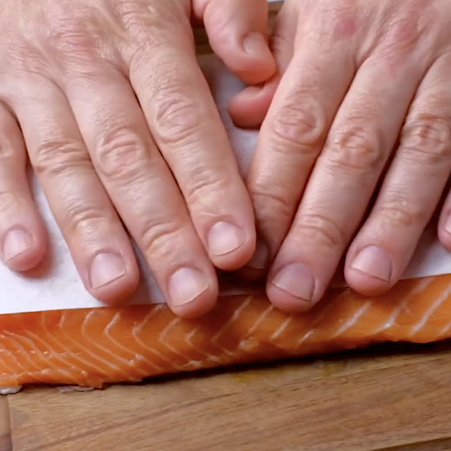 Two hands press a sheet of parchment paper onto a raw salmon fillet on a wooden surface, preparing the perfect base for a quick dinner lemon pepper salmon recipe.