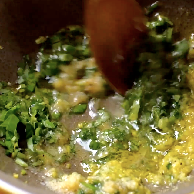 Chopped herbs, basil, and minced garlic are sautéed in oil in a pan, stirred with a wooden spoon—perfect for pairing with lemon pepper salmon.