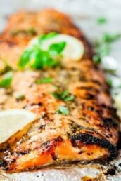 Close-up of a lemon pepper salmon fillet garnished with fresh basil and lemon slices, served on a light surface.